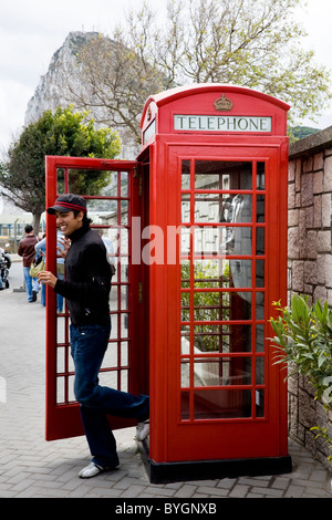 Young man / tourist leaving an original K6 red telephone / phone call box on Gibraltar, near border with Spain. Rock of Gibraltar. Stock Photo