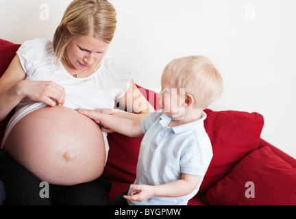 Boy touching pregnant mothers stomach on sofa Stock Photo