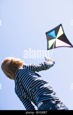 Boy flying kite in bright sunlight, against clear sky Stock Photo