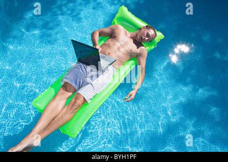 Man floating on inflatable raft with laptop and sleeping Stock Photo