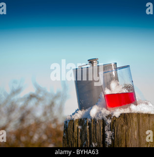 A silver hip flask and glass of sloe gin sat in the snow Stock Photo
