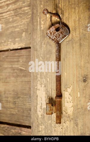 A rusty old key hanging on a nail Stock Photo