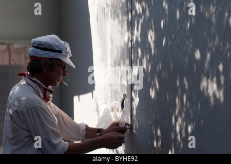 Homeowner strips masking tape from a window after painting his single family ranch style home in San Jose, CA. Stock Photo