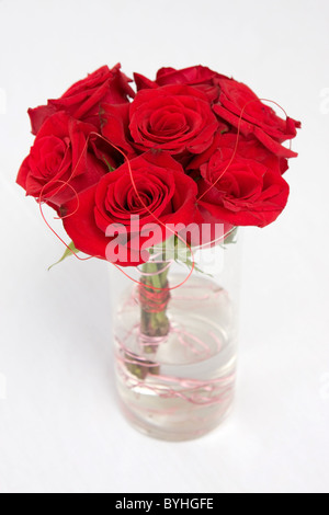 A bundle of red roses sit in water in a clear vase. Stock Photo