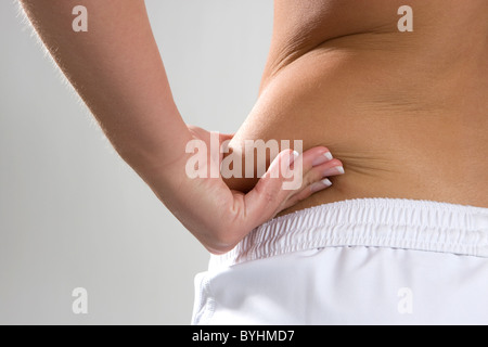 Young woman pinches the fat on the side of her waist to show the flab. Stock Photo