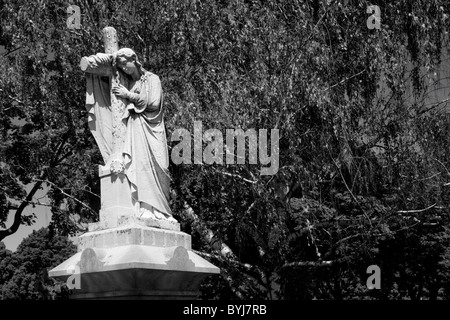 USA, Massachusetts, Lowell, Statue of Christian angel and cross atop grave in cemetery on summer morning Stock Photo