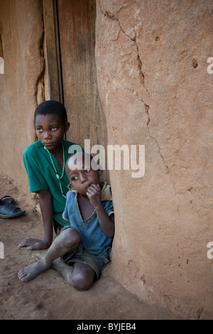 Children sit outside the doorway of their mud house in rural Masaka, Uganda, East Africa. Stock Photo