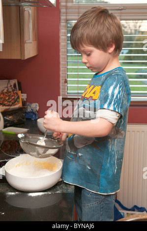 boy, child in kitchen sieving ingredients into mixing bowl making a cake .four year old Stock Photo