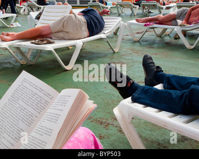 Passengers reclining on plastic sun loungers on the deck of a ship at sea Stock Photo