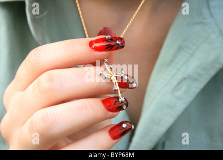 Nail-art fingers holding golden cross with necklace. Stock Photo