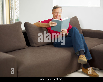 senior man reading book on sofa Stock Photo