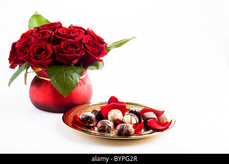 Beautiful roses in pot with gold plate of chocolates Stock Photo