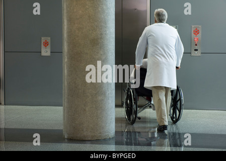 Doctor pushing patient in wheelchair toward elevator Stock Photo