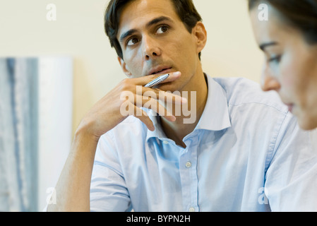 Man looking up in thought, pen in hand Stock Photo