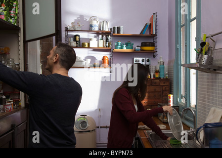 Couple in kitchen together, wife doing dishes, husband opening pantry Stock Photo