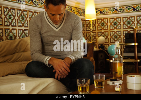 Depressed man sitting with alcohol on table Stock Photo