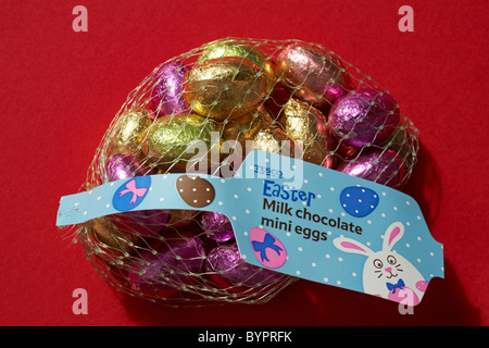 Tesco Easter milk chocolate mini eggs in foil wrappers in netting set against red background Stock Photo