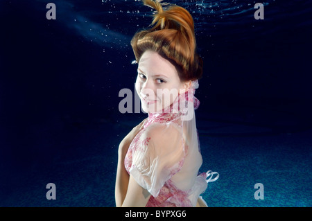 A young woman with big hair posing in a pool underwater Stock Photo