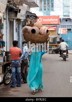 India, Rajasthan, Udaipur, woman carrying water pots in wicker basket through street Stock Photo