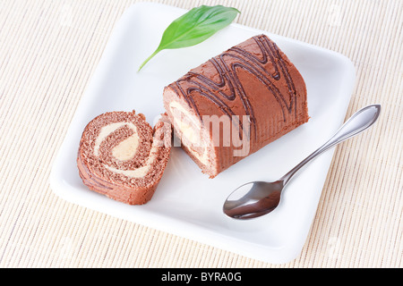 Closeup swiss roll with condensed milk cream on a white plate with spoon and a green leaf Stock Photo