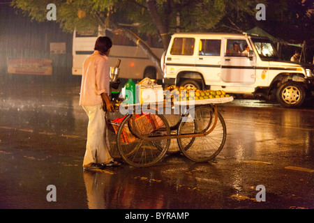 india, Uttar Pradesh, Agra orange seller with cart waiting to cross road in heavy monsoon rain Stock Photo