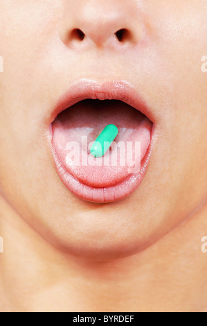 Green capsule on a young caucasian woman's tongue close up , vertical Stock Photo