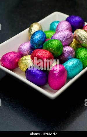 A small selection of mini chocolate eggs in a white dish on a black surface Stock Photo