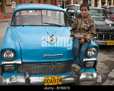 Boy sitting on a vintage taxi on the streets of Holguin, Cuba, Caribbean. Stock Photo