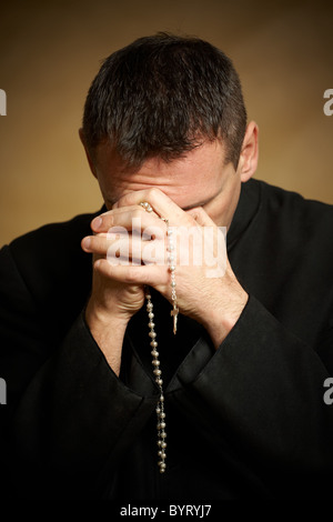 Praying priest with rosary in his hands Stock Photo