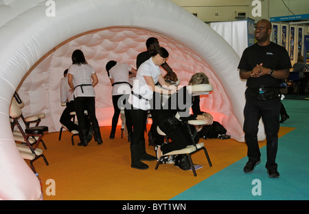 Massage therapists working from a padded cell like exhibition stand massaging visitors to a travel show in Earls Court London UK Stock Photo