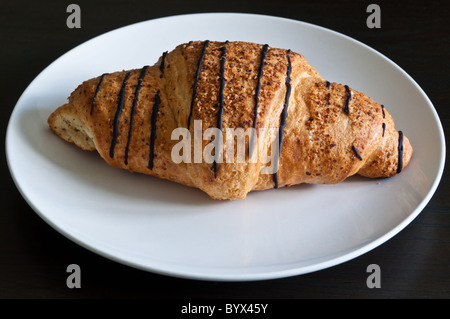 Chocolate croissant on white plate standing on dark wooden table Stock Photo