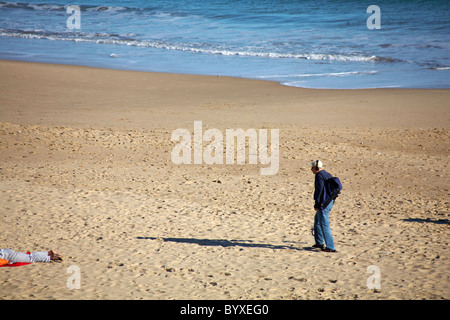 Man with metal detector equipment walking along Bournemouth Beach in the summer Stock Photo