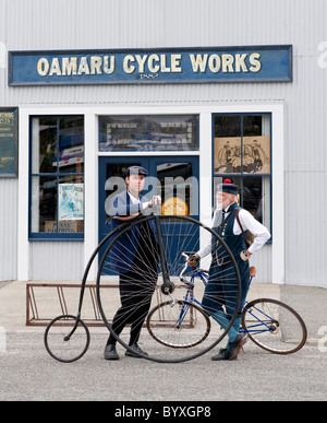 Two cyclists in period costume with a Penny Farthing bicycle outside a bike shop in Oamaru, New Zealand Stock Photo