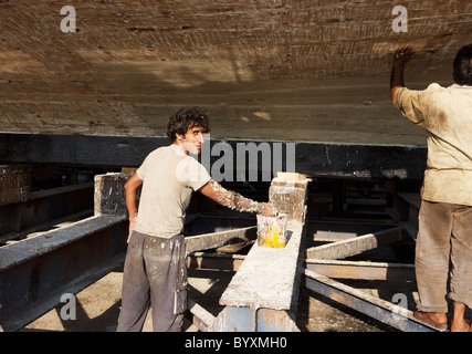 Two workers apply a sealer to the underside of a dhow in the Jaddaf boatyard, Dubai, UAE Stock Photo