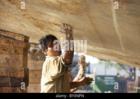 Two workers apply a sealer to the underside of a dhow, Jaddaf boatyard, Dubai, UAE Stock Photo