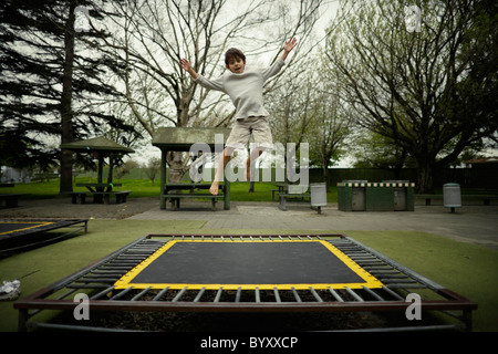 Boy bounces on trampoline in public play ground, New Zealand.