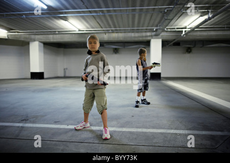 Children with stocking masks and toy guns in underground carpark prepare for big hold-up. Stock Photo