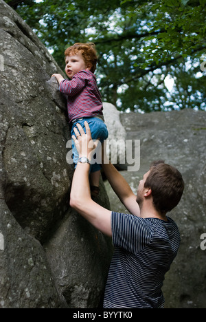 A father helps his two year old son climb a large boulder. Fontainebleau Forest, just outside Paris Stock Photo