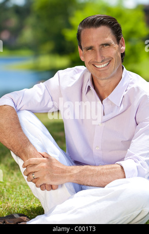 An outdoor portrait of handsome middle aged man sitting down, shot with sunlight against a natural green background Stock Photo