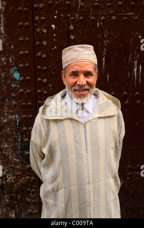 Smiling Moroccan man in djellaba and cap against an old door in el Bali Medina of Fes Morocco Stock Photo