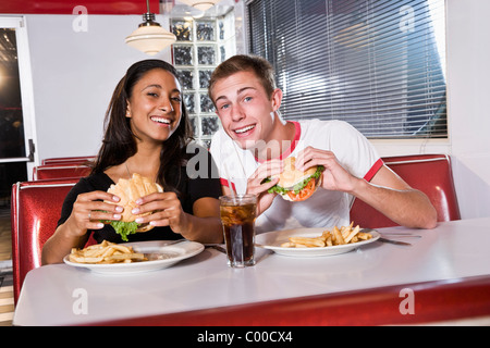 Interracial teen couple eating burgers in restaurant