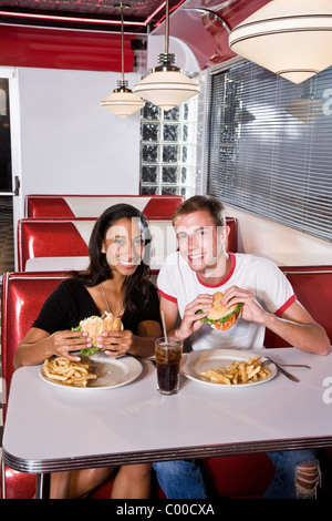 Interracial teen couple eating burgers in diner