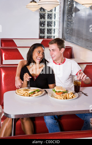 Interracial teenage couple eating burgers in diner