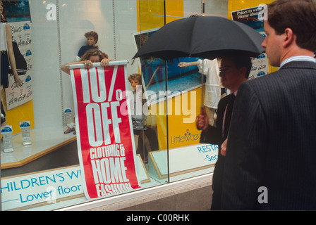 A shop assistant putting up a poster in a London shop window offering 10 percent discounts Stock Photo