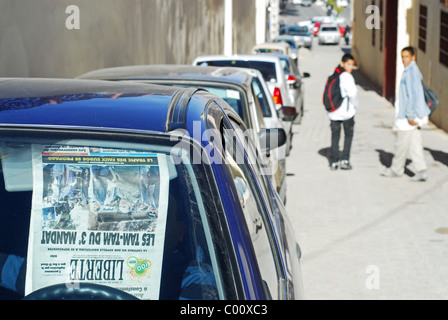 Algeria. Ghardaia, boys standing by parked cars in an alley, newspaper stucked on windscreen of one of the cars in foreground Stock Photo