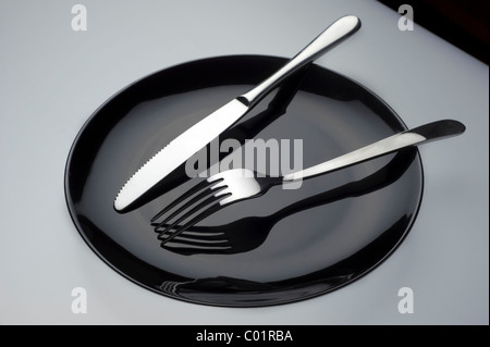 Empty black plate with knife and fork on white background Stock Photo