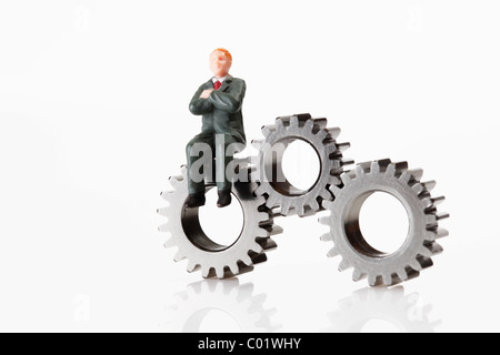 Male figurine sitting on gear wheels with arms crossed Stock Photo