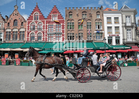 Tourists on a horse drawn carriage pass restaurants in the Grote Markt (town square) in historic Bruges (Brugge), Belgium. Stock Photo