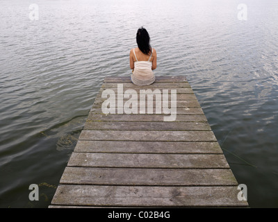 Woman sitting on a wooden pier at a lake, Mecklenburg Lake District, Mecklenburg-Western Pomerania, Germany, Europe Stock Photo