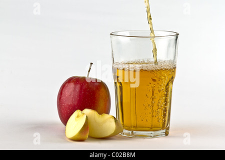 Apple cider pouring down into glass with apples at the side. On white background Stock Photo